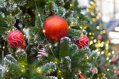 big glittery red ball ornament on christmas tree with white swirl baubles and lights background. super colorful and bright