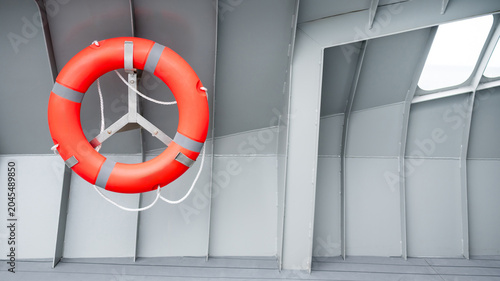 Orange lifebuoy or life preserver ring hanging on side wall of steel boat. Standard safety equipment for water rescue and emergency situations on nautical vessel.