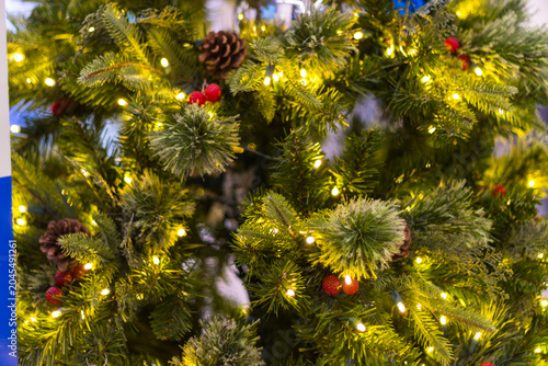 close up of a green christmas tree decorated with small warm lights pine cones and red berries