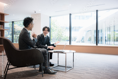 Fotografía 広いオフィスで打ち合わせをする若い営業と社長のイメージ全身　提案営業や部下の企画の説明など前向きな打ち合わせイメージ