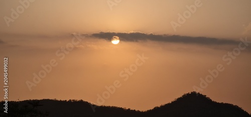 Bright Glowing Sun Setting Over Dark Silhouette of Mountain Ridge in Golden Sky