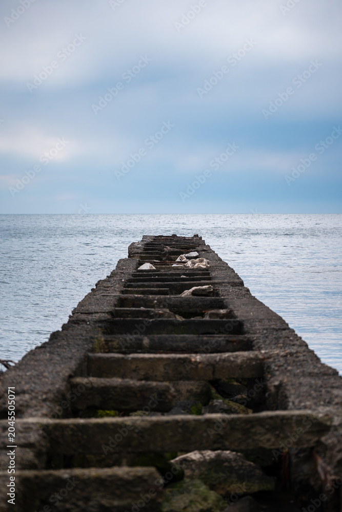 Obraz premium Old pier leading into calm water on a cloudy day