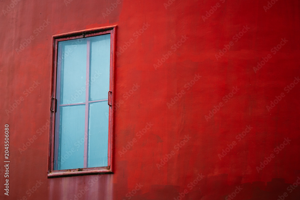 Fototapeta premium Red wall with a blue window in a simple setting during daylight hours