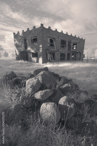 Monochrome image of an abandoned house with castellations, rock foreground, swallow-tail finials and grafitti, Australia