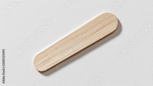 Single wooden tongue depressor medical tool for throat examination isolated on a light textured background top view
