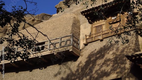 Traditional Wooden Balconies on Cliffside Rock Facade in Sunlight