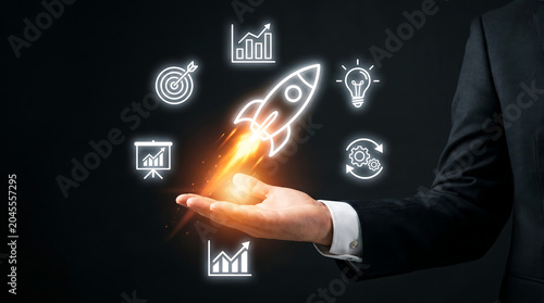 Businessman hand holding glowing rocket icon, startup growth symbols, finance charts, and target goal, on dark background