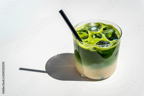 An iced matcha latte with oat milk resting on a white background table in a glass