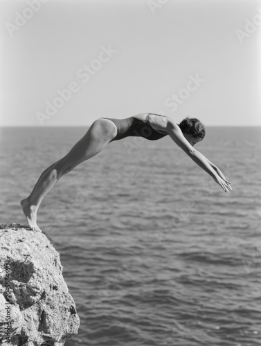 Black and white photo of a woman in a swimsuit diving headfirst from a rocky cliff into the sea, capturing freedom, adventure, summer travel and outdoor coastal lifestyle.