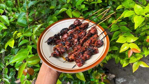 Foto close up view of goat or beef satay served on a plate and holding by the hand