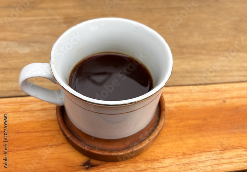 A cup of hot black coffee in a white ceramic mug on a wooden saucer and table background