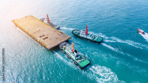 Billede på lærred Tugboats towing a large empty flat deck barge through the turquoise ocean