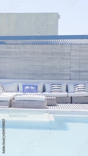 Vertical video: Shifting sunlight causing pool water rippling by wicker sofa with ottoman, pillows