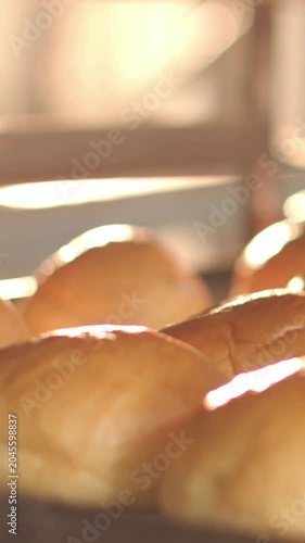 Vertical video: Pushing cam, moving as backlight shifting on bakery tray, showing rolls' glossy top