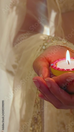 Vertical video: Flame drawing woman at home wearing cream sari, holding diya with pink rim for puja