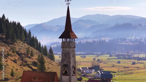 Aerial drone view of a tall wooden church tower rising above a scenic valley in Bucovina, Romania