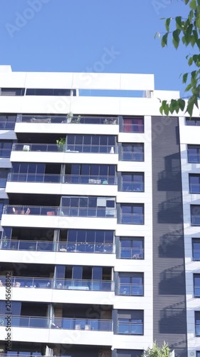 A daytime low-angle vertical shot of the iconic Mirador building in Madrid, Spain. The contemporary residential tower features high-contrast white, dark grey, and red panels with a massive open centra