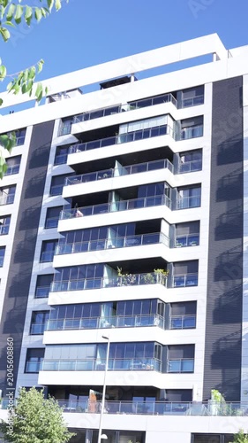 Vertical view of a modern residential apartment building with glass balconies and contemporary urban architecture under a clear blue sky in Madrid, Spain.