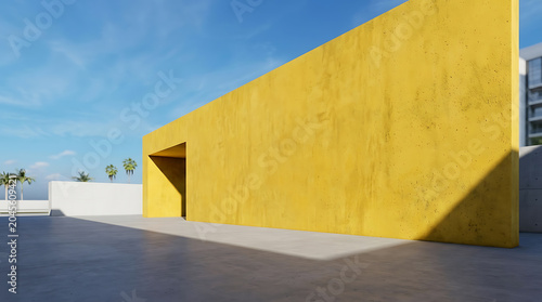 A large vibrant yellow concrete wall stands prominently against a bright blue sky on a sunny day 