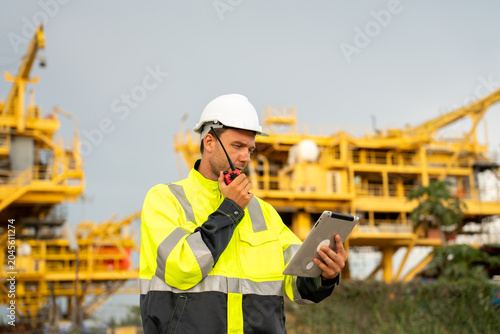 Canvastavla Industrial engineer using a walkie-talkie radio and holding a digital tablet at an offshore energy platform facility