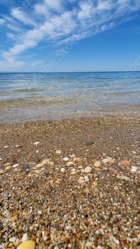 Pebble Beach With Clear Waves and Distant Island on a Calm Summer Day