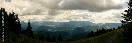 Fotografie Dramatic view of expansive mountain landscape under cloudy sky with forested slo