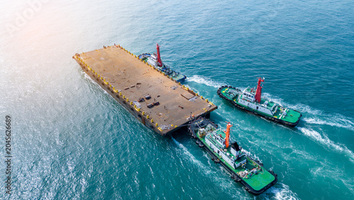Bild auf Leinwand Tugboats towing a large empty flat deck barge through the turquoise ocean