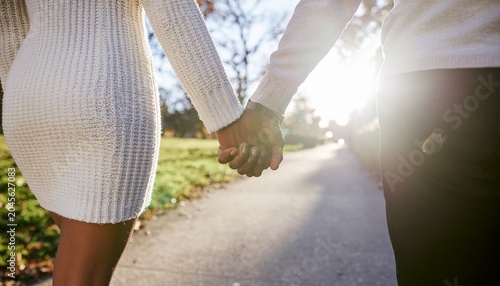 oung couple holding hands while walking through city park, genuine connection