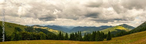 Tableau sur toile Expansive panoramic view of rolling green hills and mountain ridges with dramati