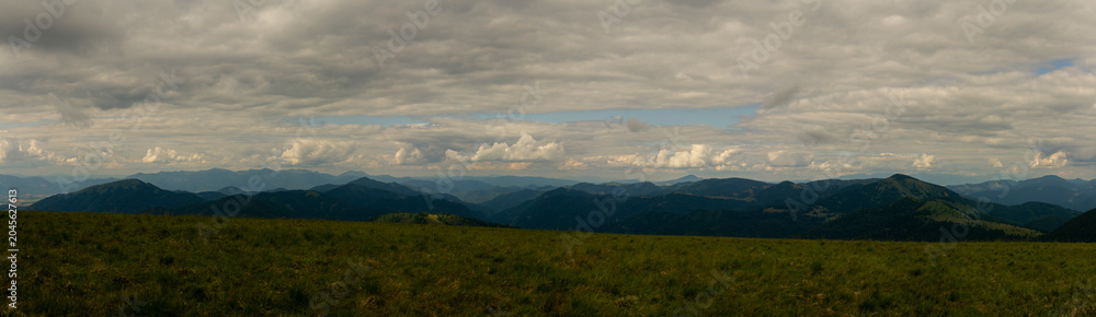 Obraz premium Majestic panoramic view over rolling green mountain ridges under dramatic cloudy sky in summer daylight landscape