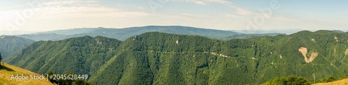 Panoramic view showcasing expansive forested hills, deep valleys and distant blue mountains under partly cloudy skies