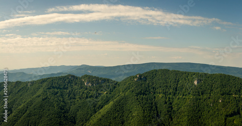 Wide panoramic view of lush green forested hills and distant layered ridgelines beneath dramatic summer sky