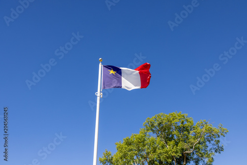 Acadian flag flying on a white flagpole against a clear blue sky in Nova Scotia Canada celebrating Acadian heritage and cultural identity.