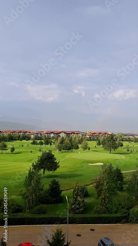 Rainbow Over Lush Golf Course With Green Fairways, Trees, and Distant Homes Under a Dynamic Sky