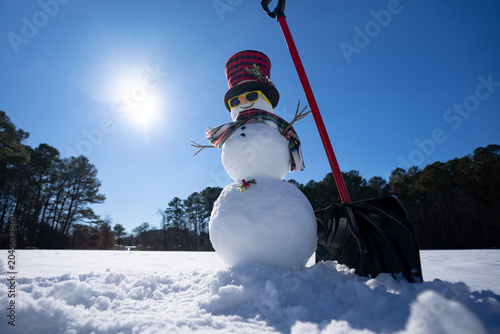 Winter design with snowman and snow shovel. Winter snowman with shovel clearing snow outdoors. Winter outdoor scene with snowman. Cute snowman with snow shovel and wooden vintage sled in winter field.