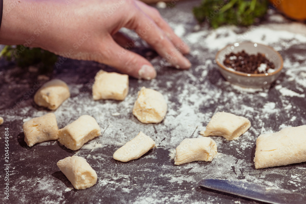 Fototapeta premium Hand Cutting Gnocchi Dough Pieces on Floured Surface During Homemade Gnocchi Preparation