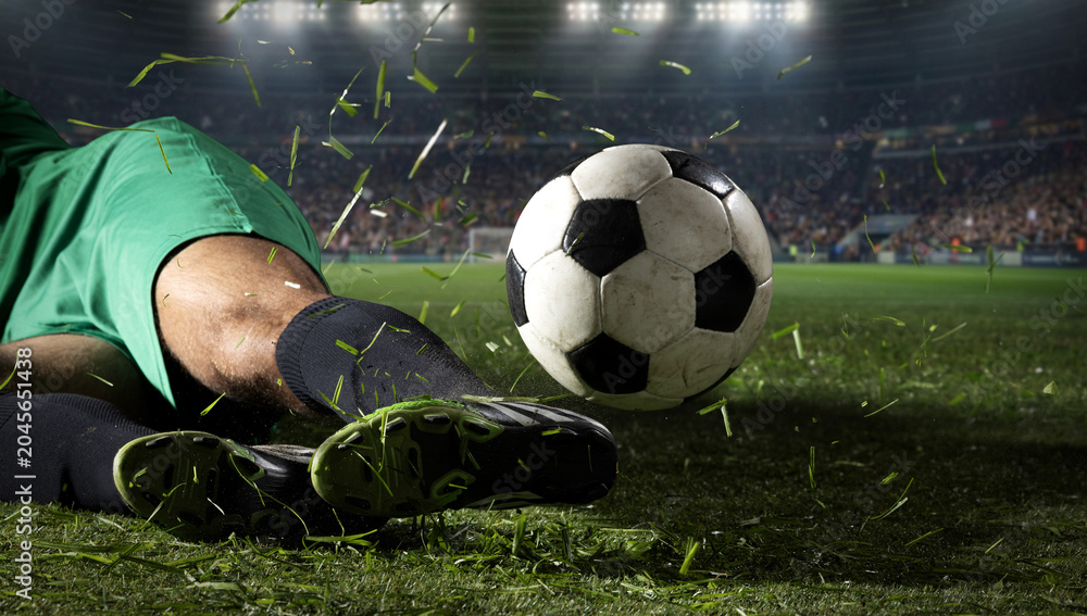 Naklejka premium Soccer ball flying after slide tackle on grass field with stadium lights. Concept of defensive play, match drama, sports news, tournament ads, and dynamic football media.