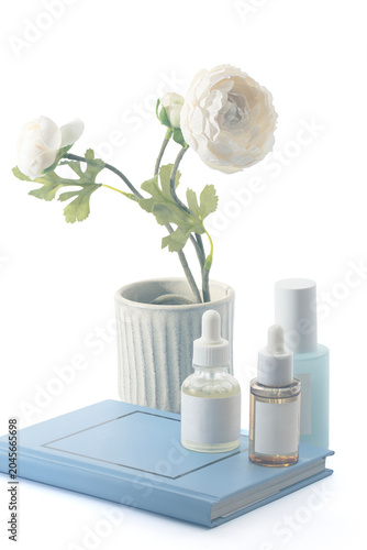 A soft, high-key shot of facial serums and a blue spray bottle resting on a notebook. A white flower bloom adds a fresh, botanical feel to this seasonal beauty promotion.