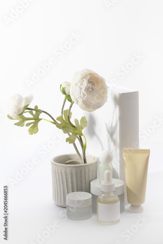 Elegant arrangement of cosmetic containers with blank labels against a white book. Perfect for showcasing spring discounts on hydrating and rejuvenating skincare products.
