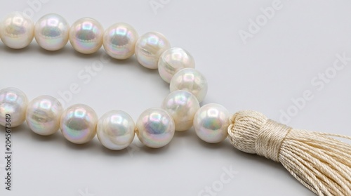 Close-up of white freshwater pearl necklace with natural jute tassel on neutral background