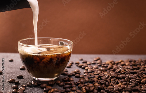 Coffee beans scattered around a glass of coffee on a dark surface