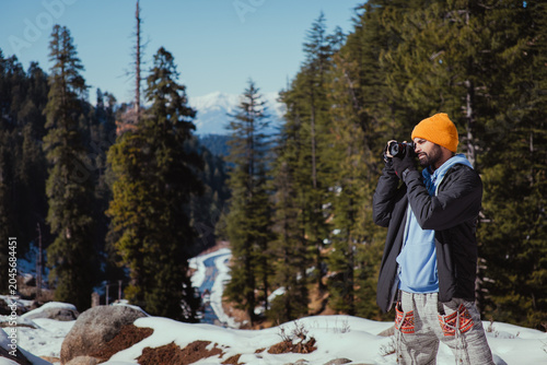 Photography Photographer capturing scenic mountain views in a snowy pine forest during a bri