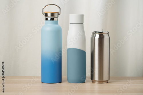 Blue and White Insulated Water Bottles and Stainless Steel Travel Can on Wooden Table