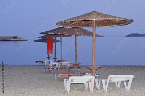 Perspective row of straw umbrellas and sunbeds on a peaceful beach at sunset