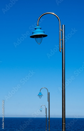Tableau sur toile Vertical image of three streetlights diminishing in the distance, with the sea i
