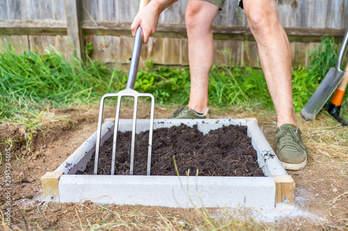 Foto Person using a garden fork to loosen and distribute soil inside a newly built ra