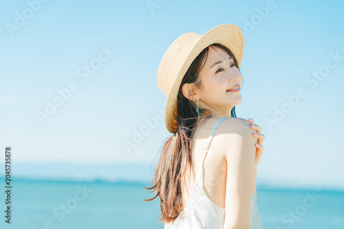 Fotografía 海と青空バックの麦わら帽子を被った女性