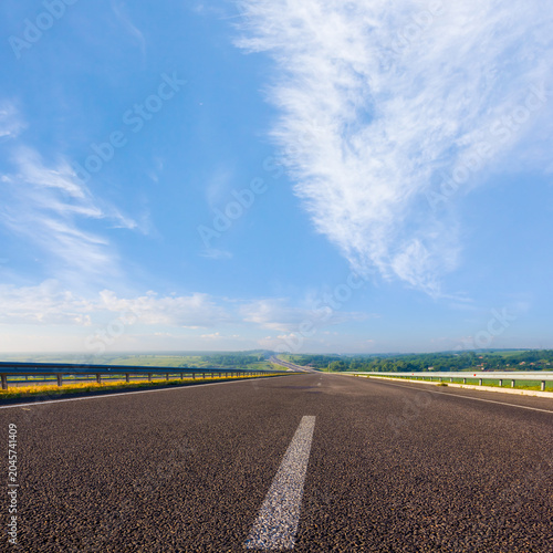 long asphalt road among green fields under blue cloudy sky