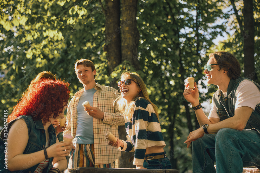 Obraz premium Cheerful young friends with ice cream laughing in park with retro effect. Concept of weekend joy, candid emotions, outdoor gathering, summer leisure, and friendly conversation.