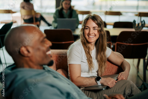 Diverse colleagues laughing during conversation while sitting on couch at coworking space